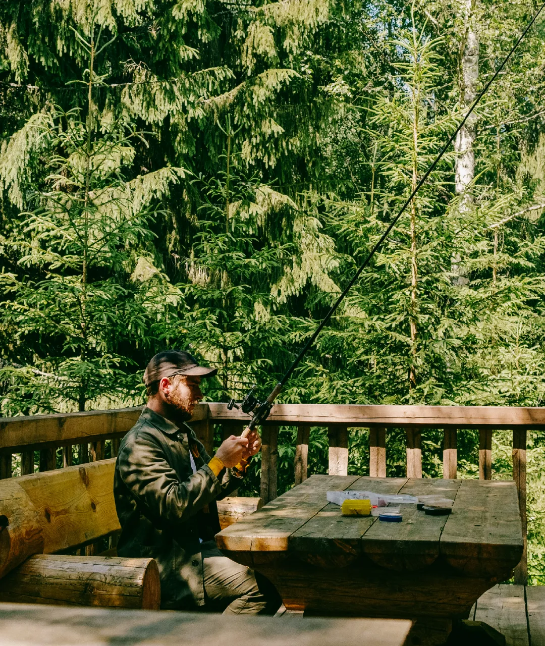 Person fishing from a wooden deck surrounded by evergreen trees.