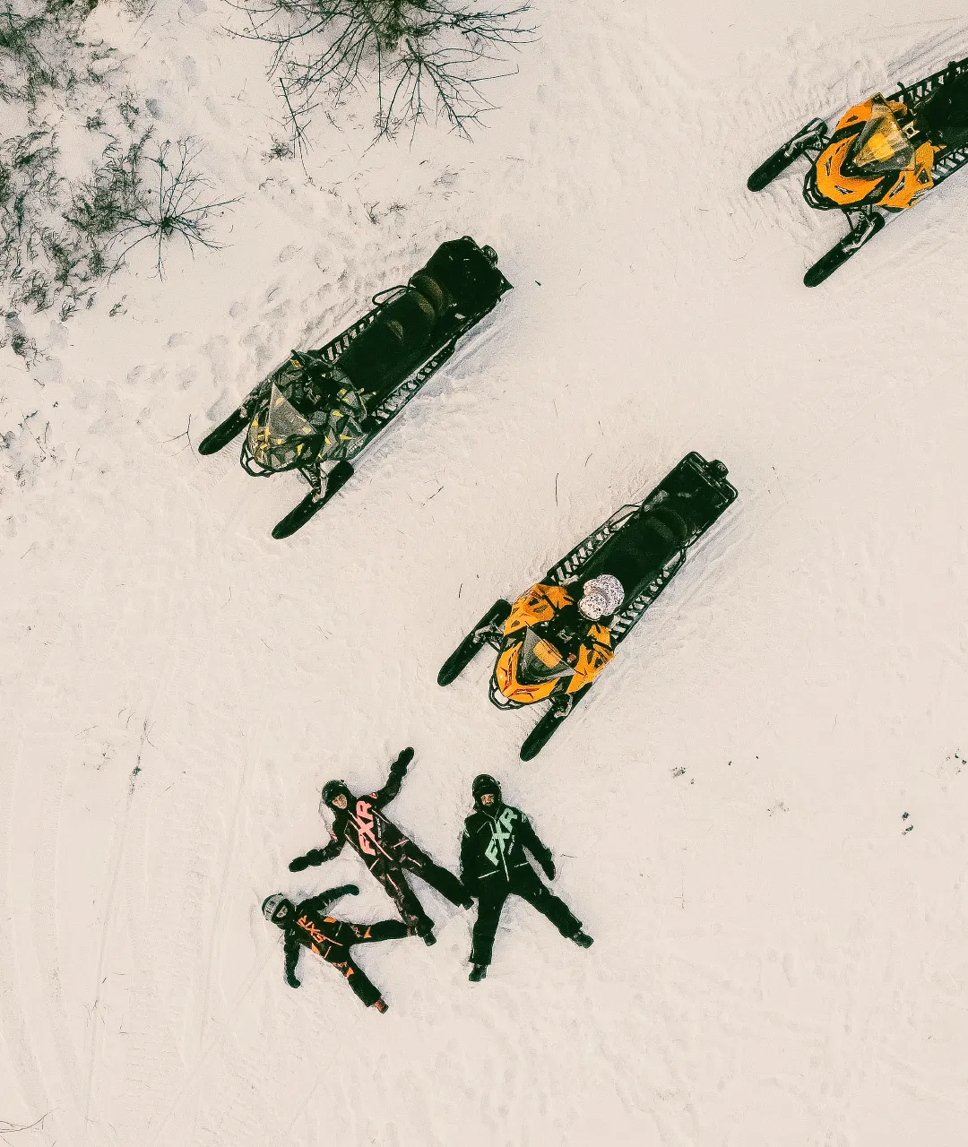 Overhead view of snowmobiles and riders resting on a snowy trail.