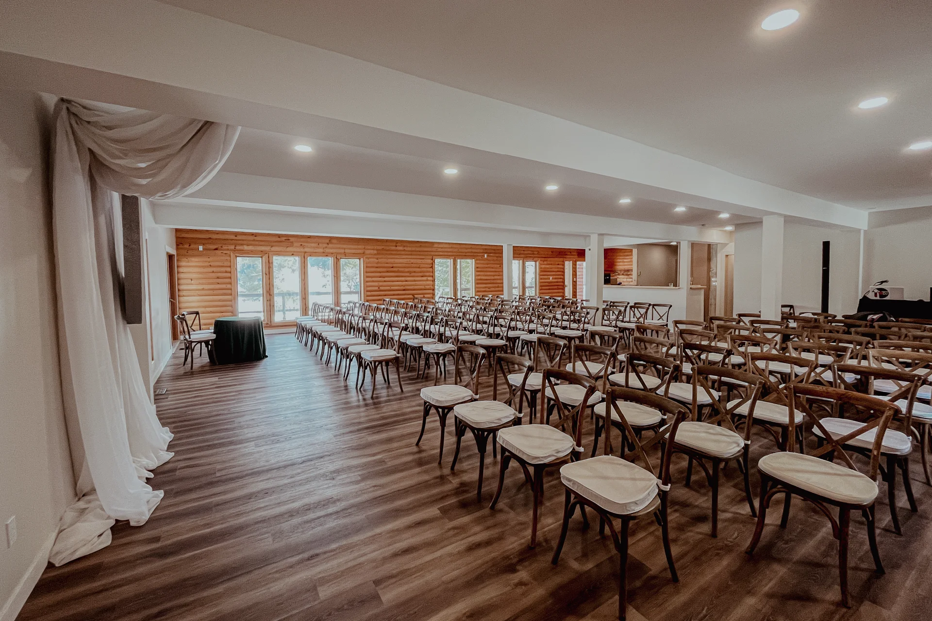 Spacious lodge event room arranged with rows of chairs, wood-paneled walls and a ceremony table.