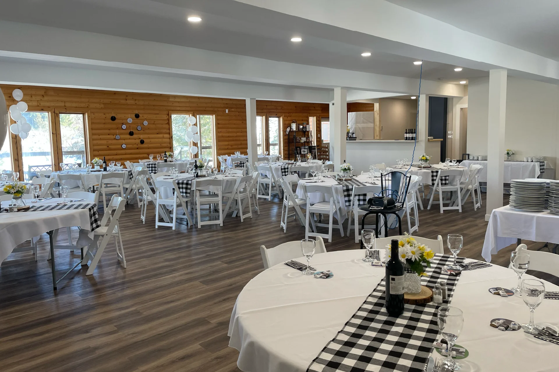 Event room set with round tables, white chairs, black-and-white checkered runners and simple flower centrepieces.
