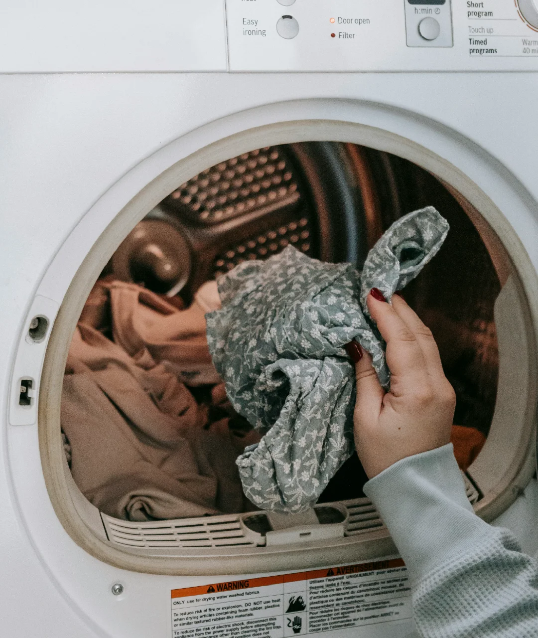 Hand placing clothing into the open door of a front-load dryer.