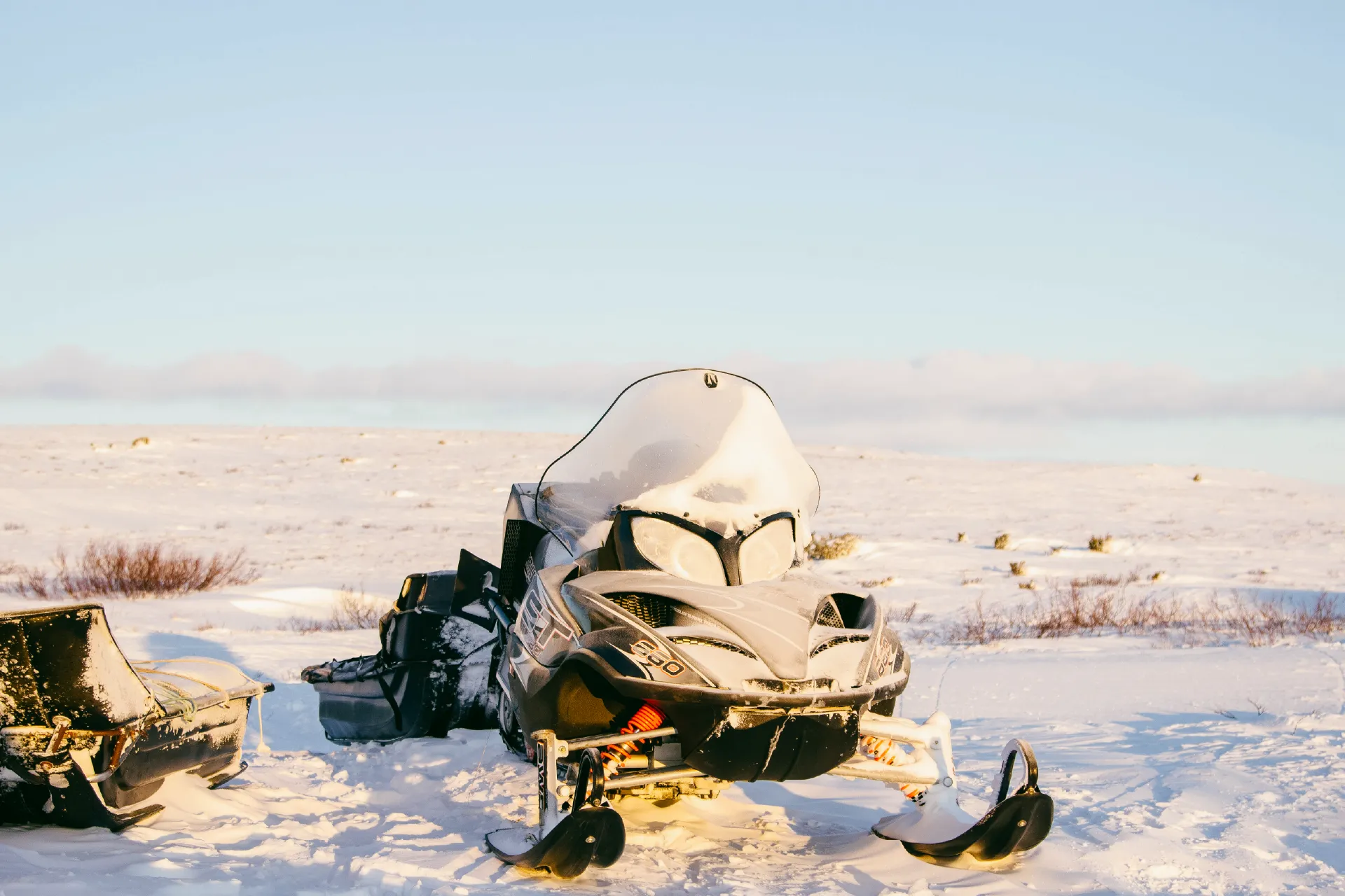 Snowmobile parked on a snowy landscape with a sled attached.