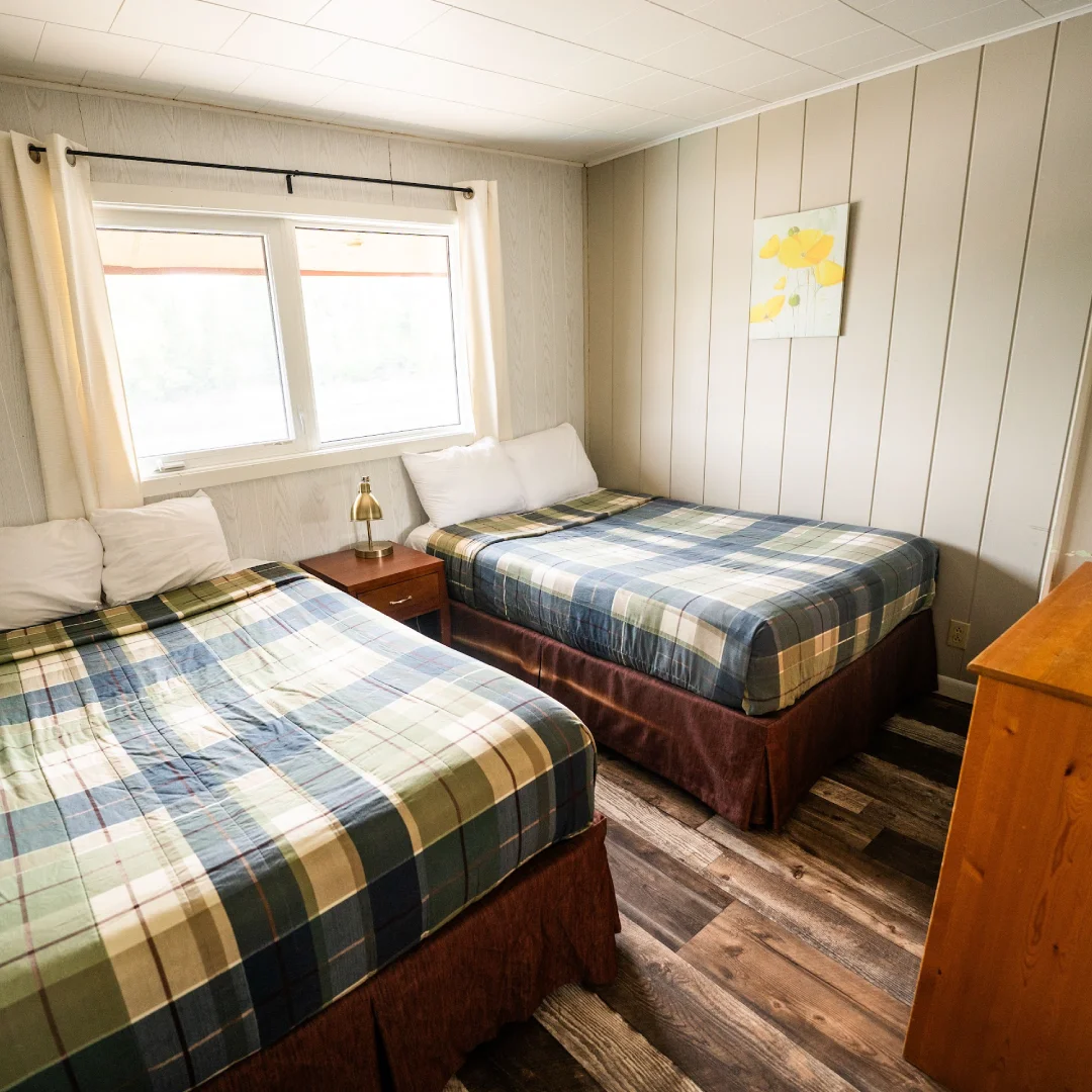 Cabin bedroom with two beds, plaid blankets, a nightstand, and a window.