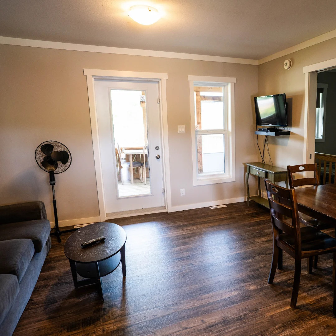 Cabin living and dining area with a sofa, coffee table, wall-mounted TV, dining table, and door leading to the screened porch.