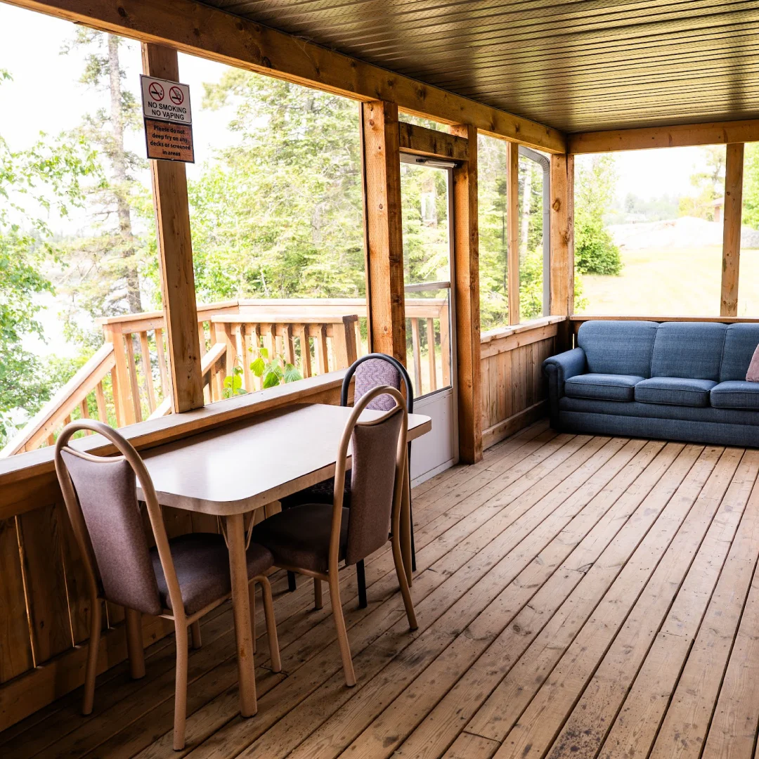 Exterior of the Beachfront Cabins with a covered wooden porch, string lights, large rocks, a barbecue, and a truck parked in front.