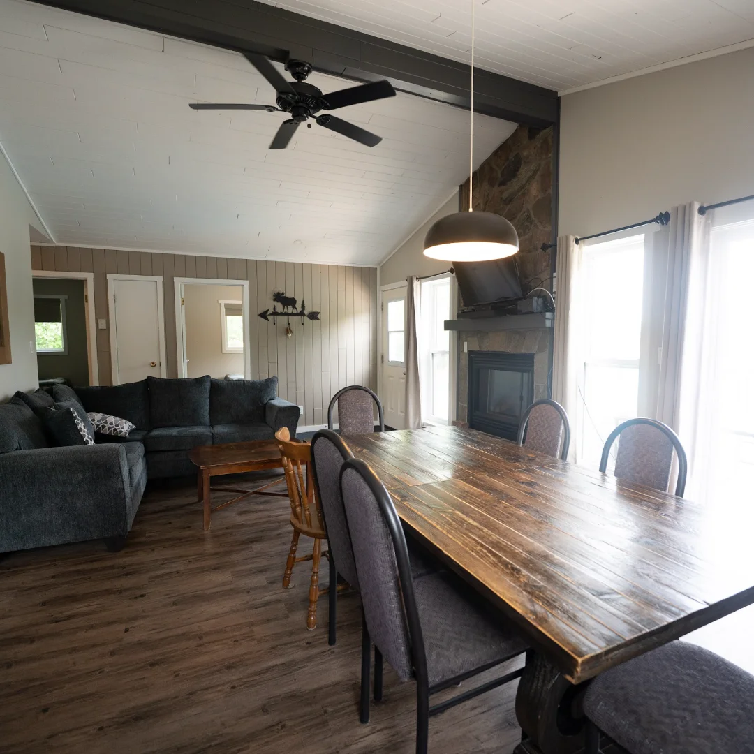 Open living and dining area inside the Dam View Cabin with vaulted ceiling, stone fireplace, sofas, and wood table.