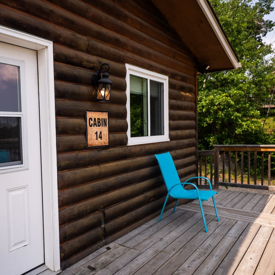 Interior of the Perch Bay Dam View Cabin with grey sofas, a wooden dining table, stone fireplace, and bright windows.