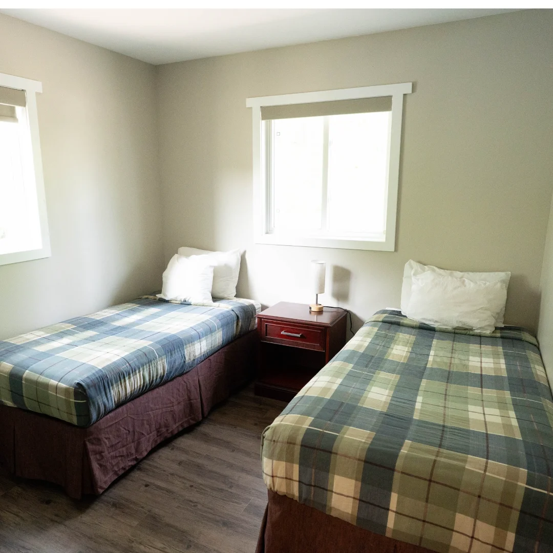 Bedroom in the Perch Bay Dam View Cabin with two single beds, plaid bedding, a nightstand, and two bright windows.