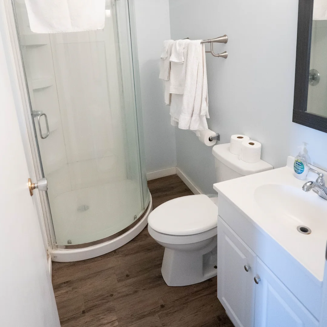 Bathroom in the Perch Bay Dam View Cabin with a corner shower, white vanity, toilet, towels, and wood-look flooring.