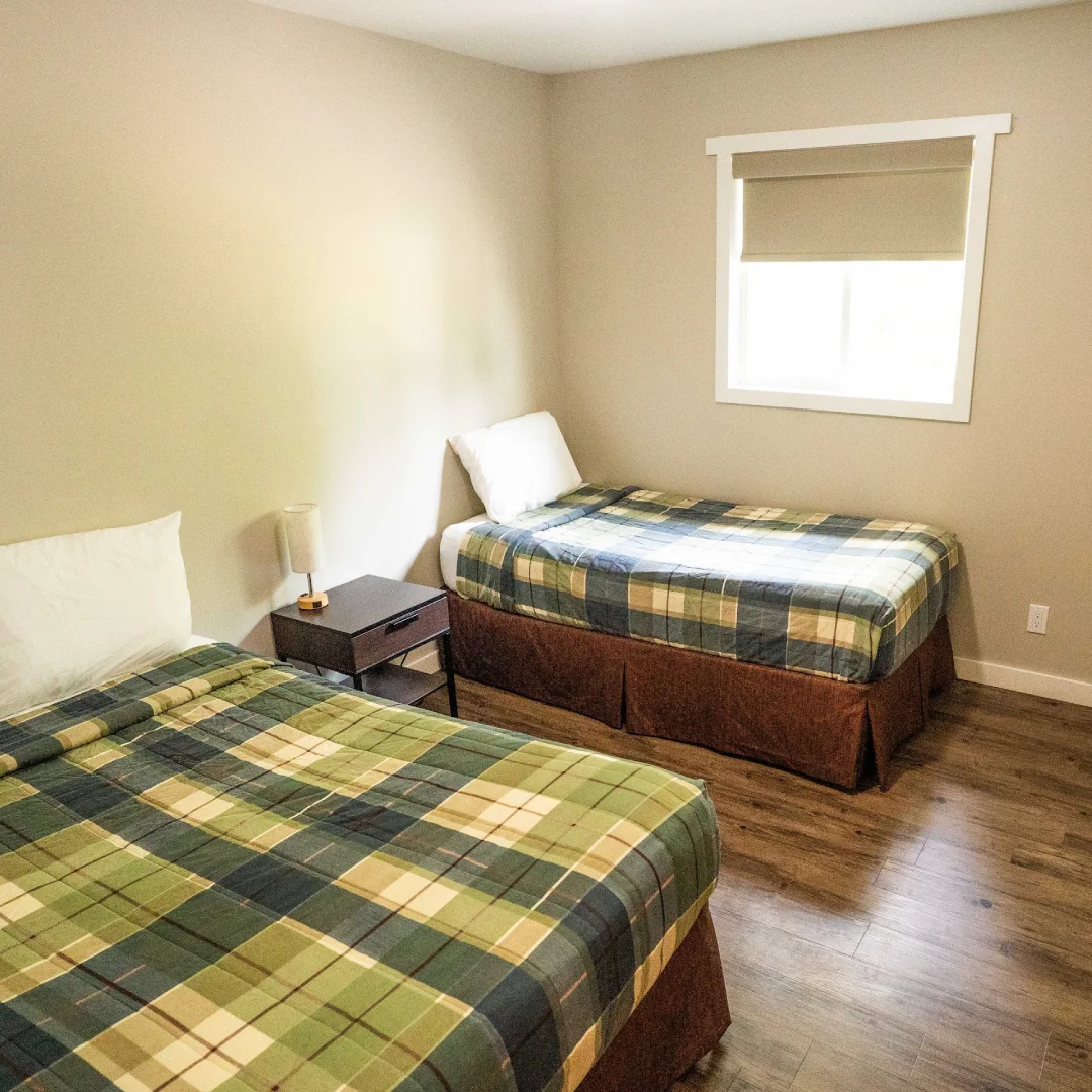 Bedroom in the Perch Bay Dam View Cabin with two single beds, plaid bedding, a nightstand, and two bright windows.