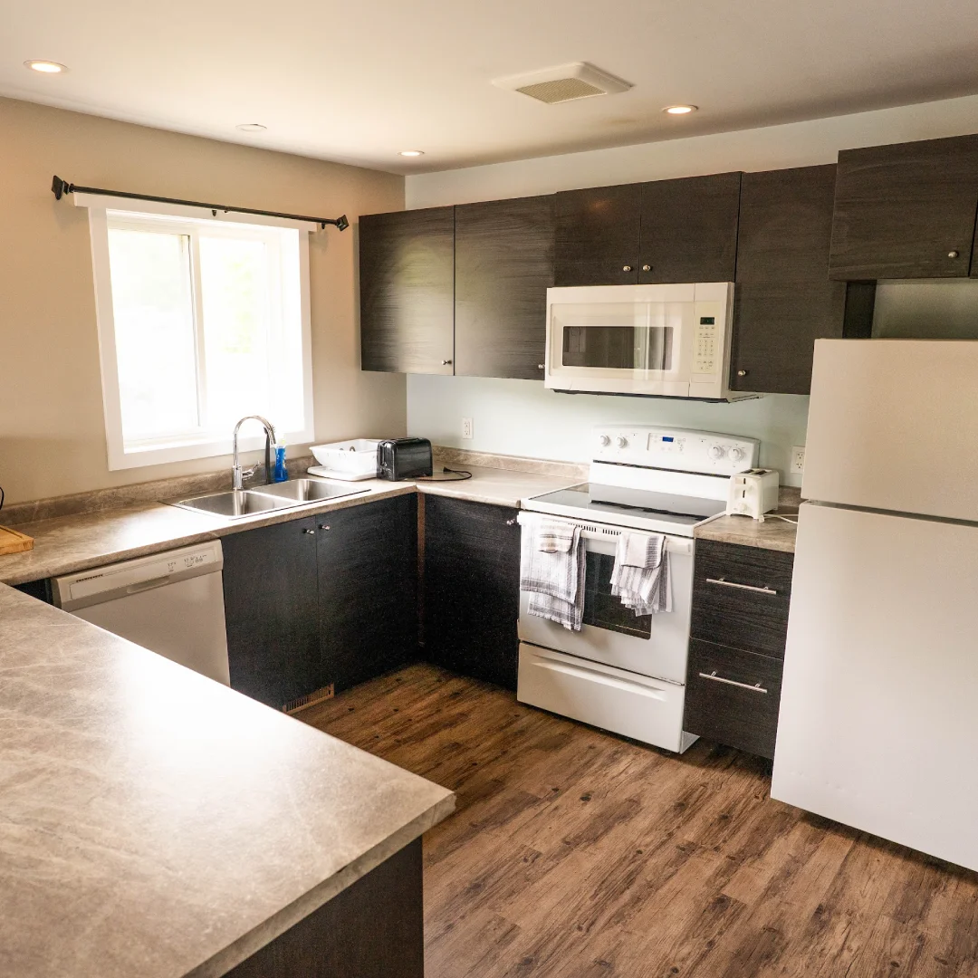 Full kitchen inside the Perch Bay Dam View Cabin with dark cabinets, white appliances, sink, microwave, and window.