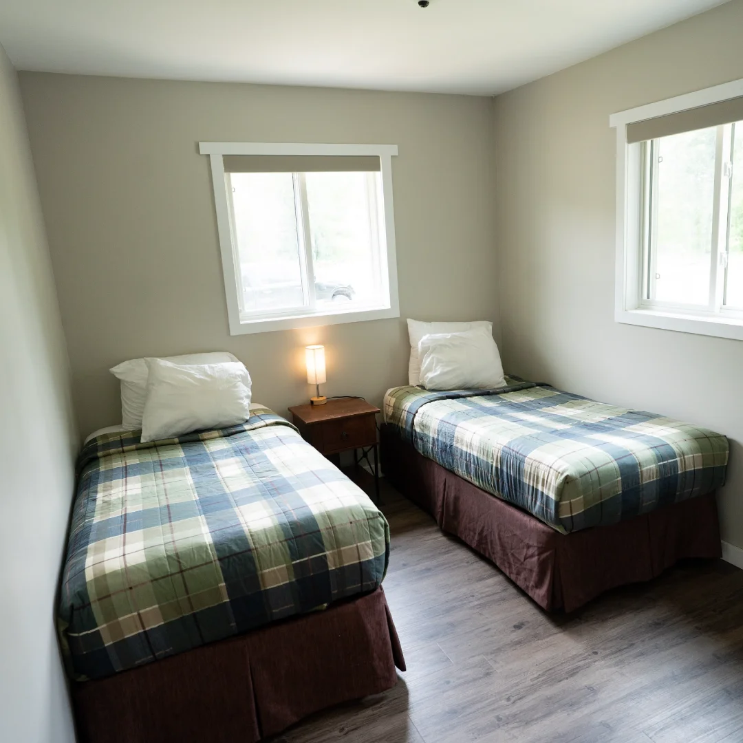 Twin bedroom in the Dam View Cabin with two single beds, plaid bedding, white pillows, and a small lamp between beds.