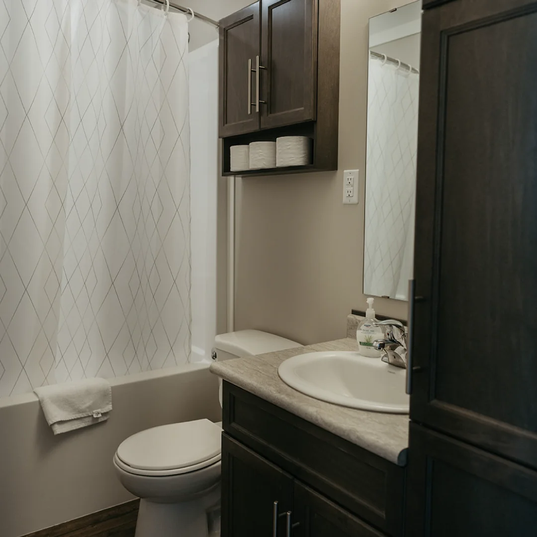 Bathroom in the Perch Bay Harbour Cabin with a bathtub and shower curtain, toilet, sink, mirror, and dark storage cabinets.