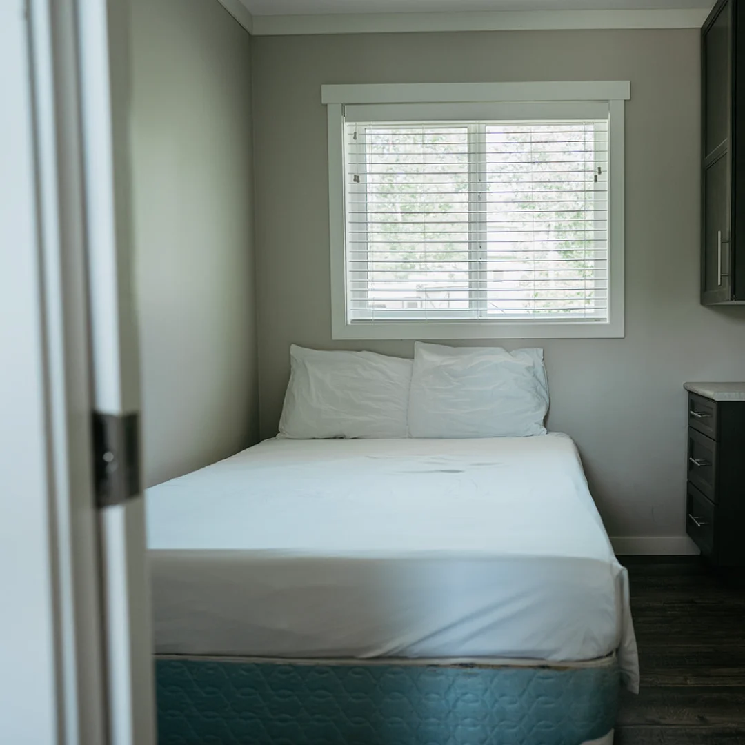 Bedroom in the Perch Bay Harbour Cabin with a double bed, white bedding, window blinds, and dark built-in storage.