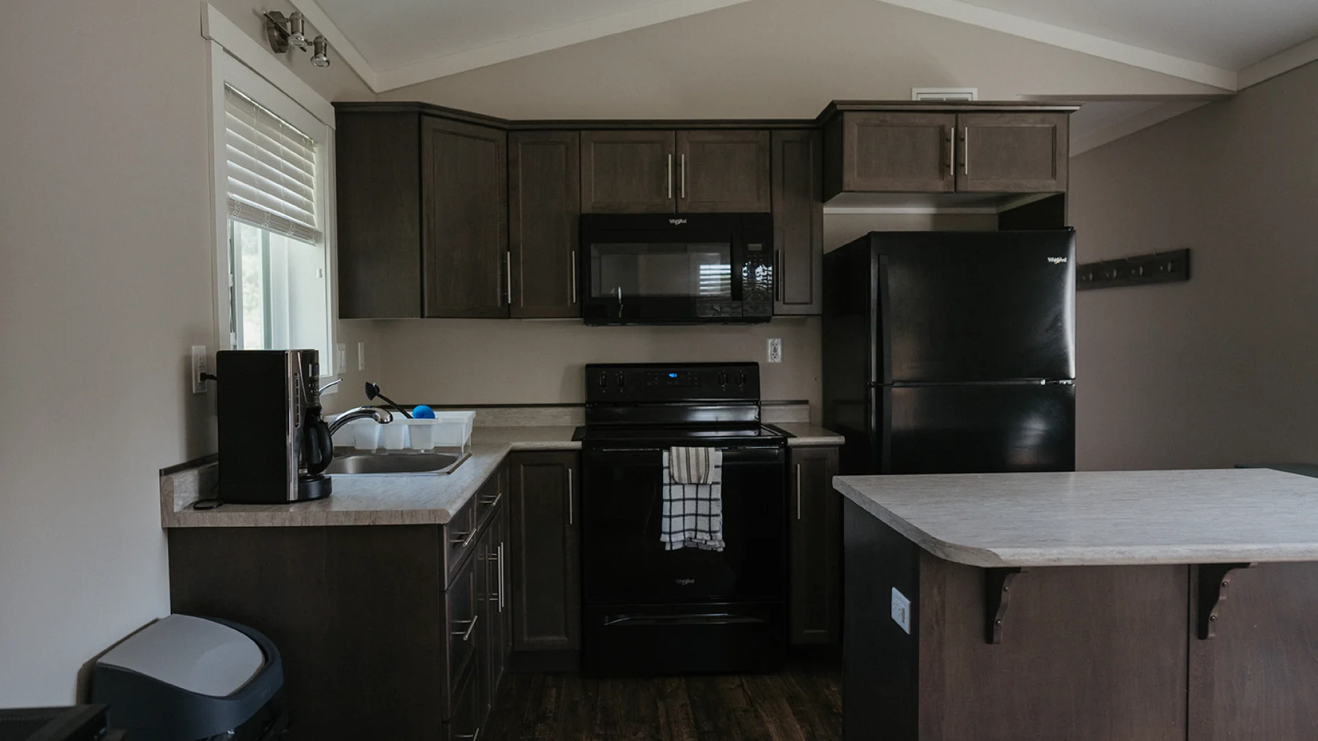 Kitchen inside the Perch Bay Harbour Cabin with dark cabinets, black appliances, a sink, coffee maker, and island counter