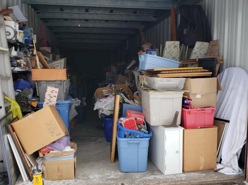 Storage unit filled with stacked boxes, plastic bins, and miscellaneous household items.