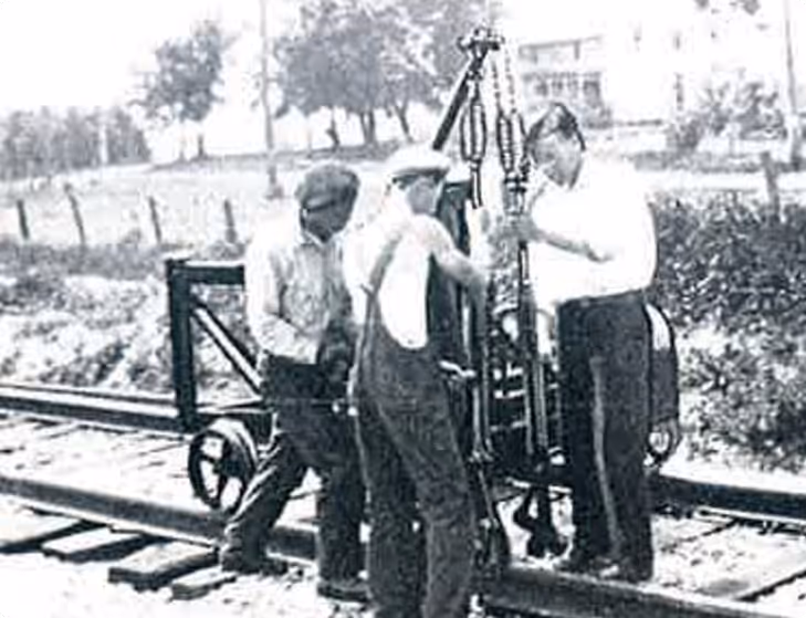 Close-up of a mechanical component with red springs, positioned above railroad track gravel and a wooden railroad tie.