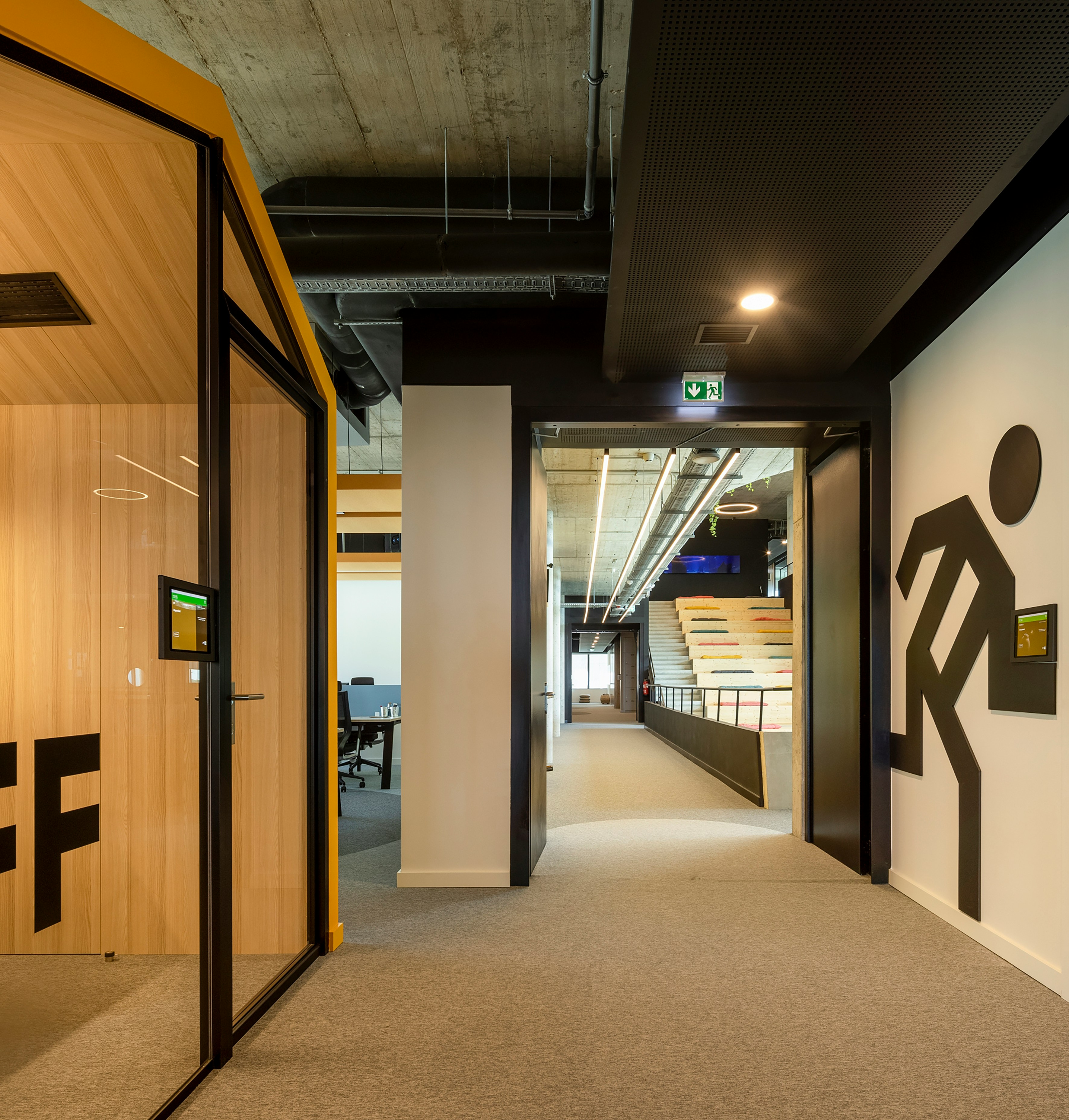 Modern office hallway with open doors, glass walls, and a stepped seating area at the end.