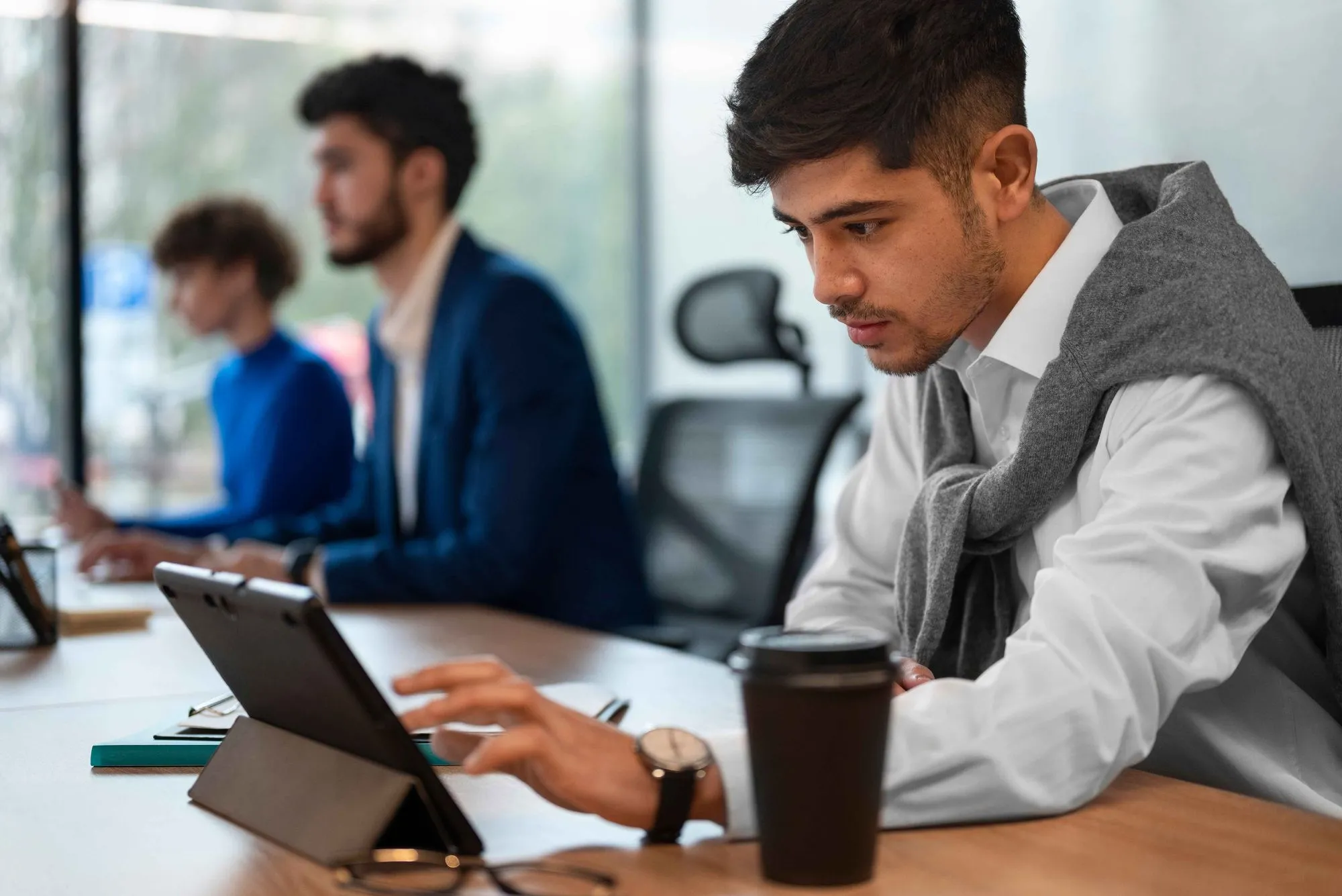 A man wearing a blue jacket is typing on a laptop.