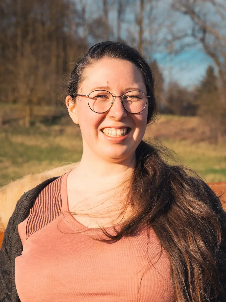 Eine Frau steht lächelnd vor einem Pferd. Die Frau ist Katharina.