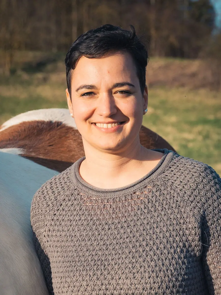 Eine Frau steht lächelnd vor einem Pferd. Die Frau ist Kathrin.