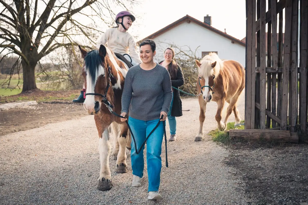 Ein Kind sitzt lachend auf einem Pferd. Das Pferd wird geführt.