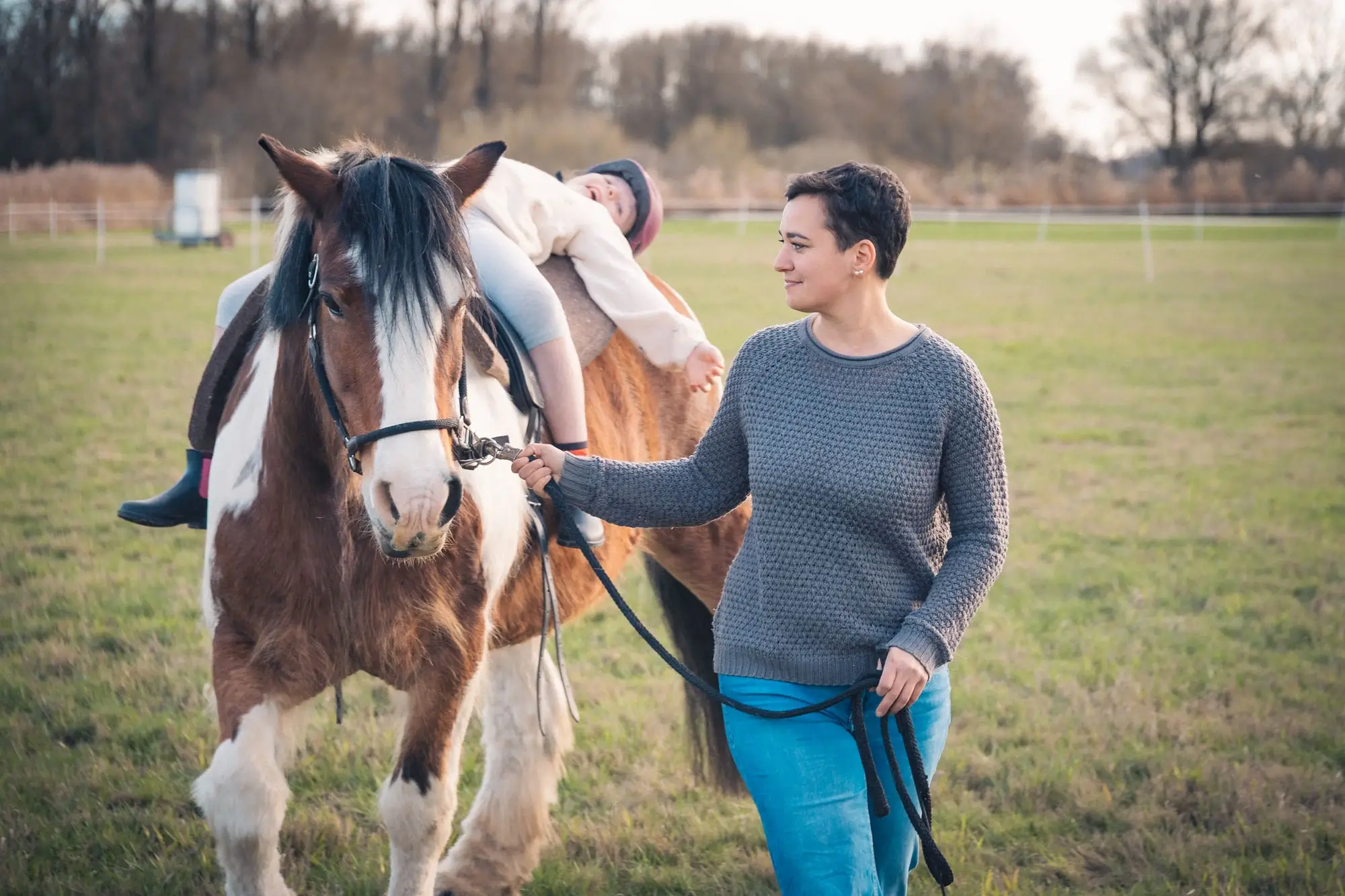 Kind liegt auf dem Rücken eines Pferdes. Das Pferd wird geführt.