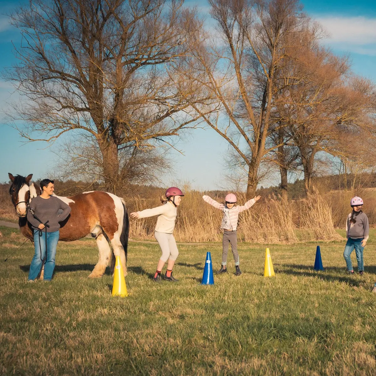 Zwei Pferde und drei Kinder spielen auf einer Wiese. Die Kinder machen Hampelmänner.