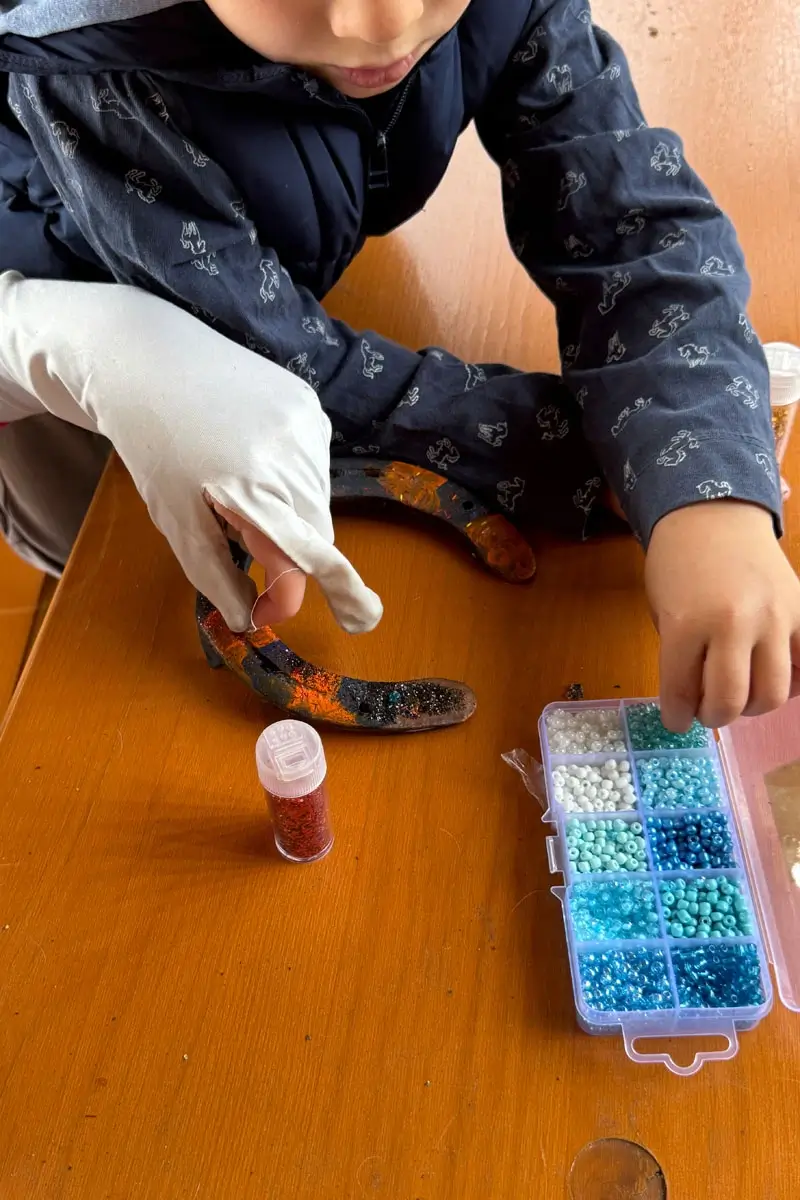 Zwei Kinder sitzen an einem Tisch und basteln Hufeisen mit Glitzer und Perlen.