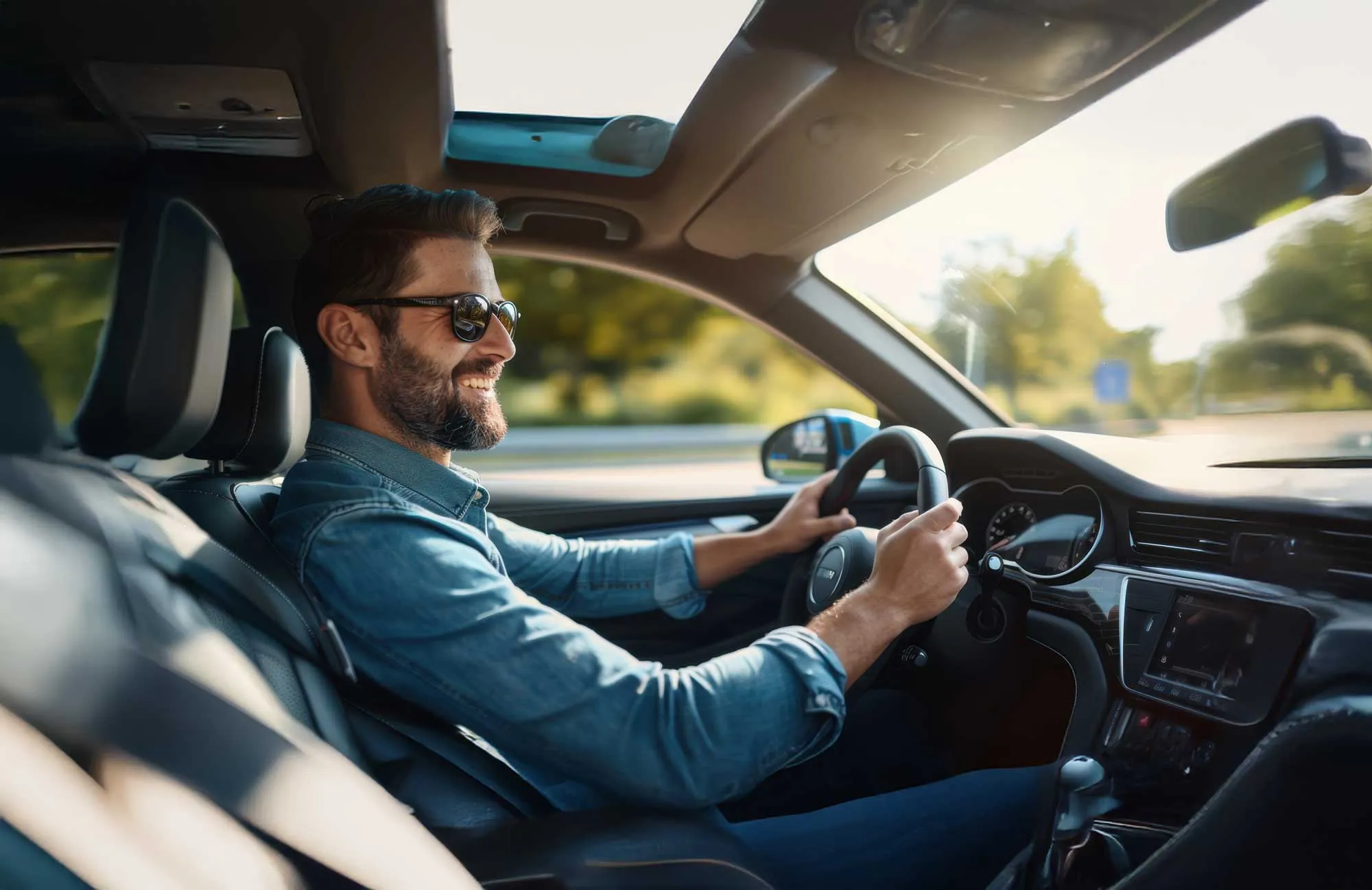 Smiling man wearing sunglasses driving a car with sunroof on a sunny day.
