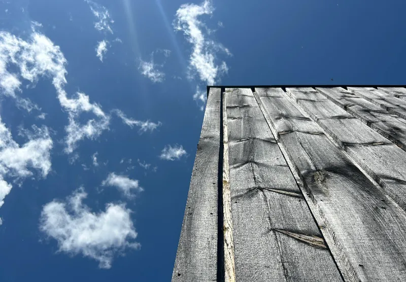 A weathered wooden wall against a blue sky with scattered clouds.