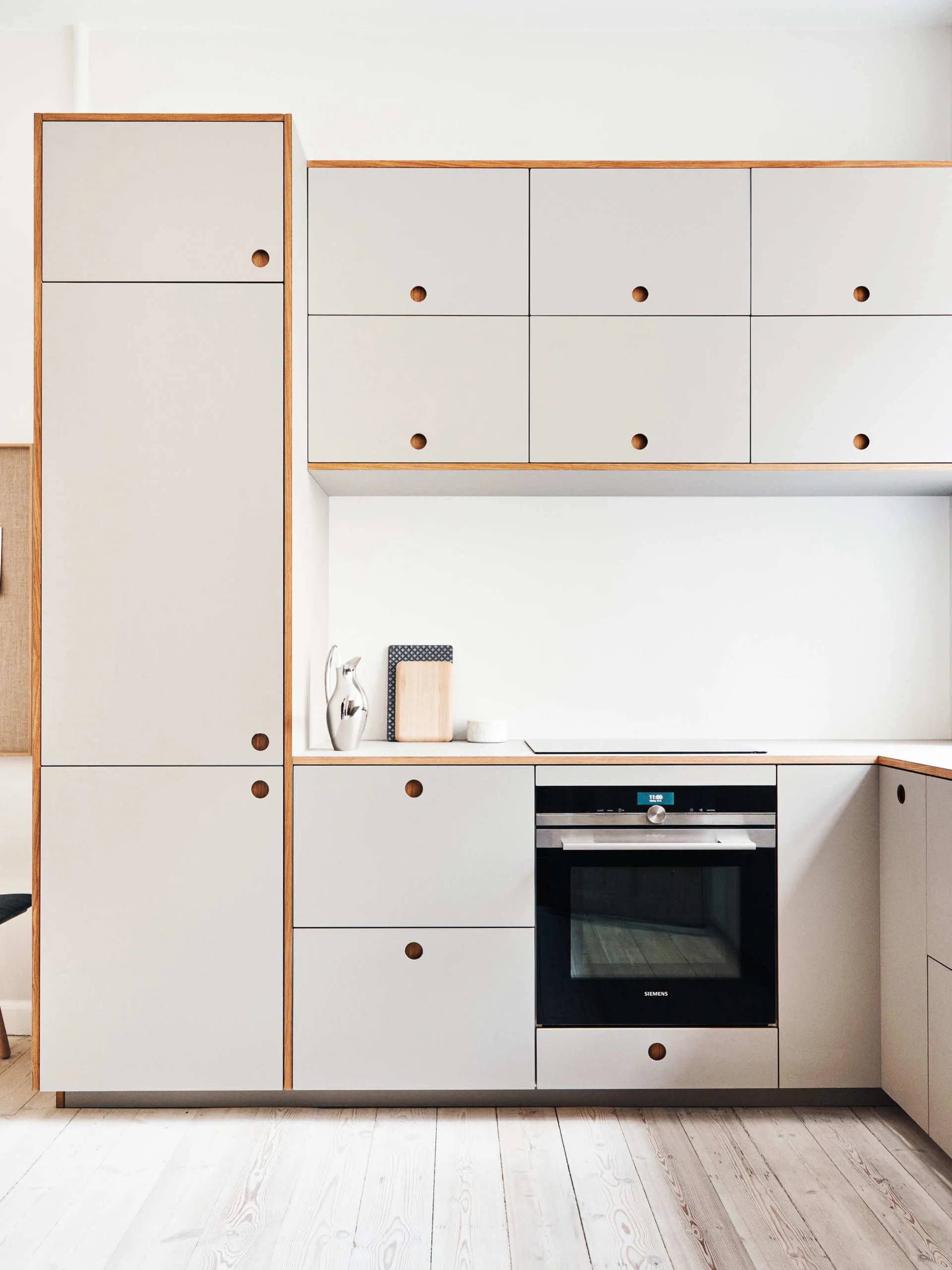 Modern kitchen with light gray cabinets, built-in Siemens oven, and light wood flooring.