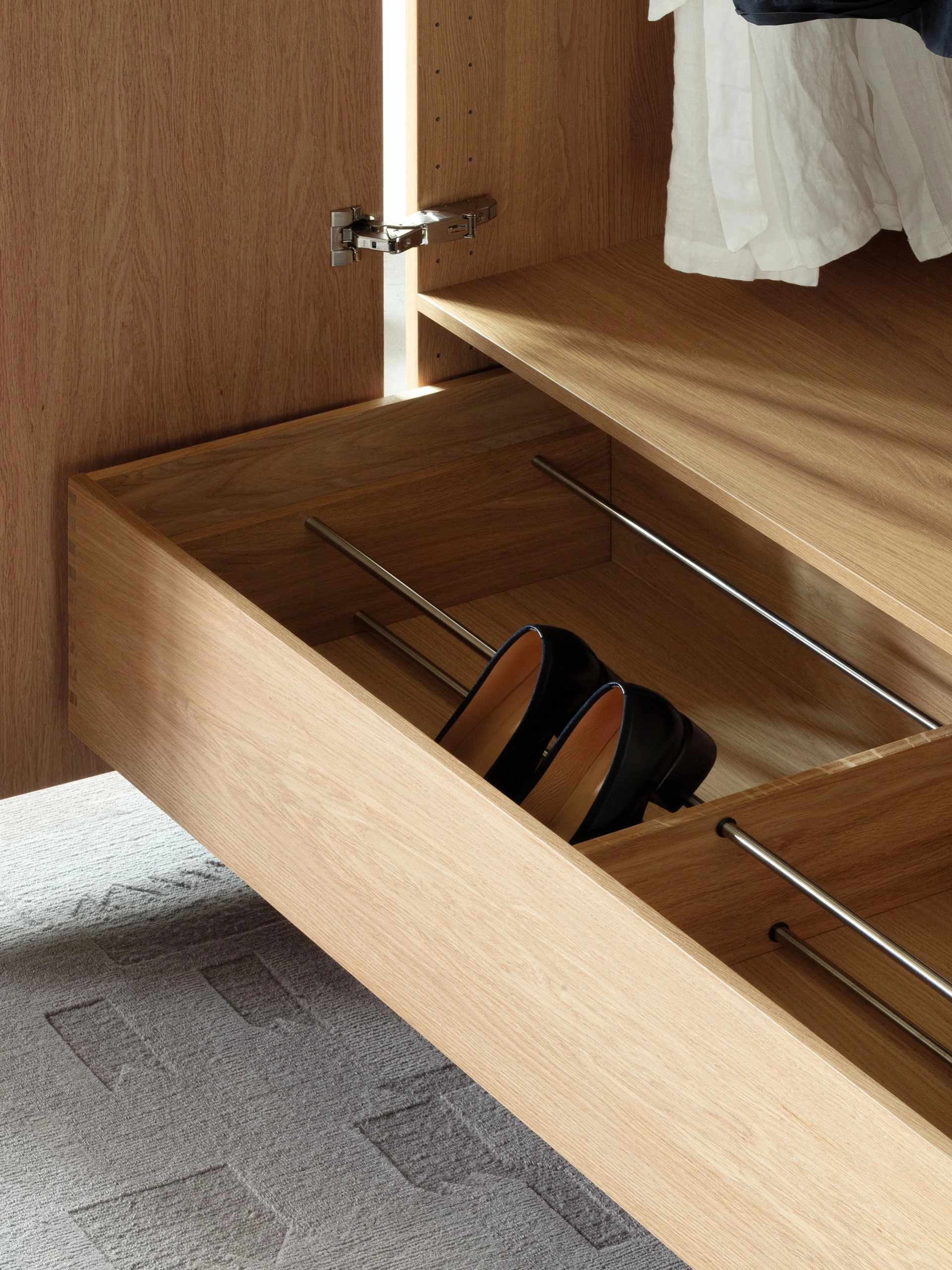 Open wooden drawer in a wardrobe with metal shoe rack rods.