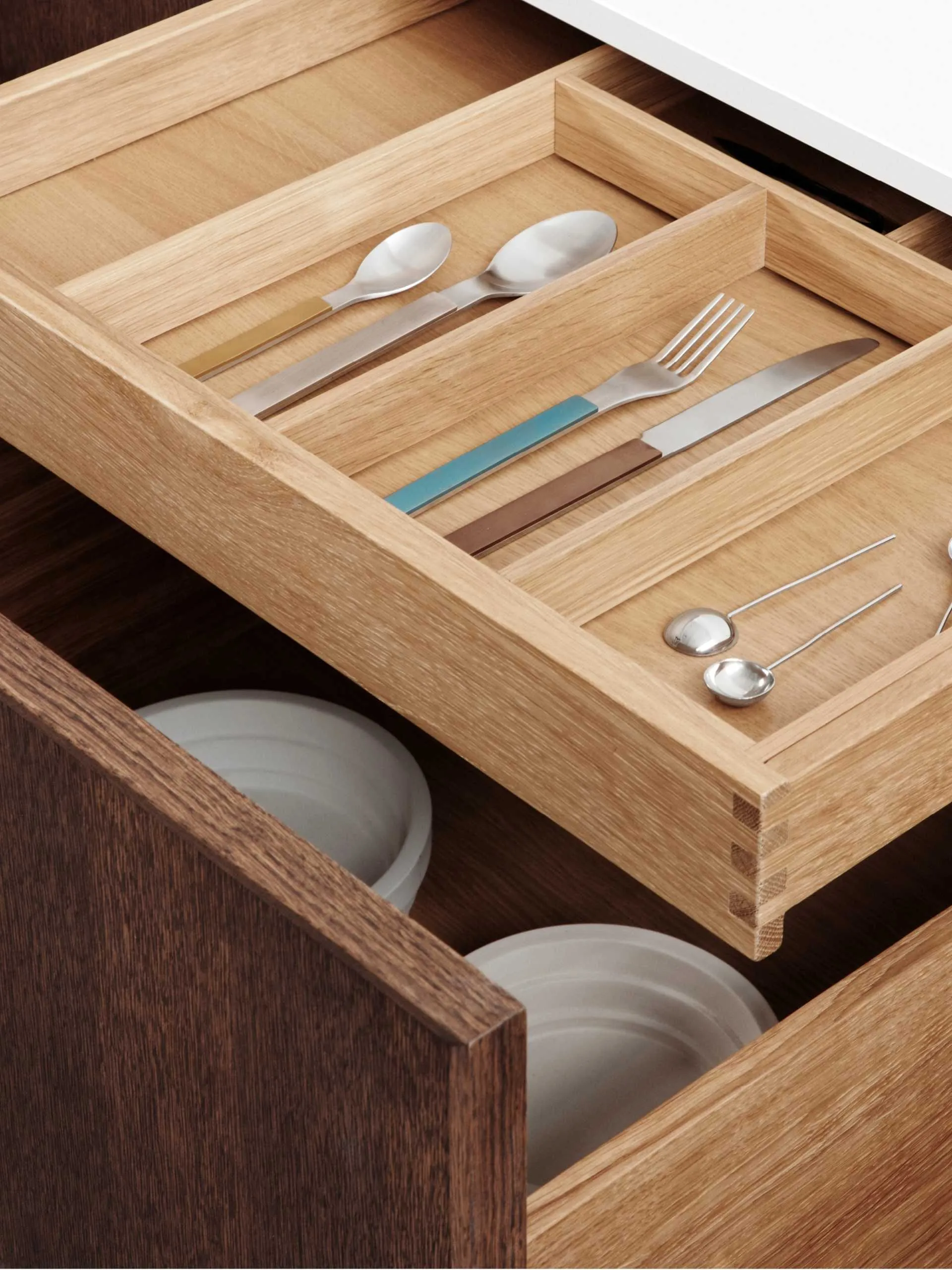Open wooden kitchen drawers with slide-out cutlery organizer, and drawer of stacked plates below.