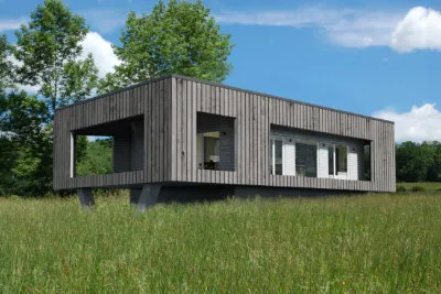 Modern elevated wooden house with large windows in a grassy field under a blue sky.