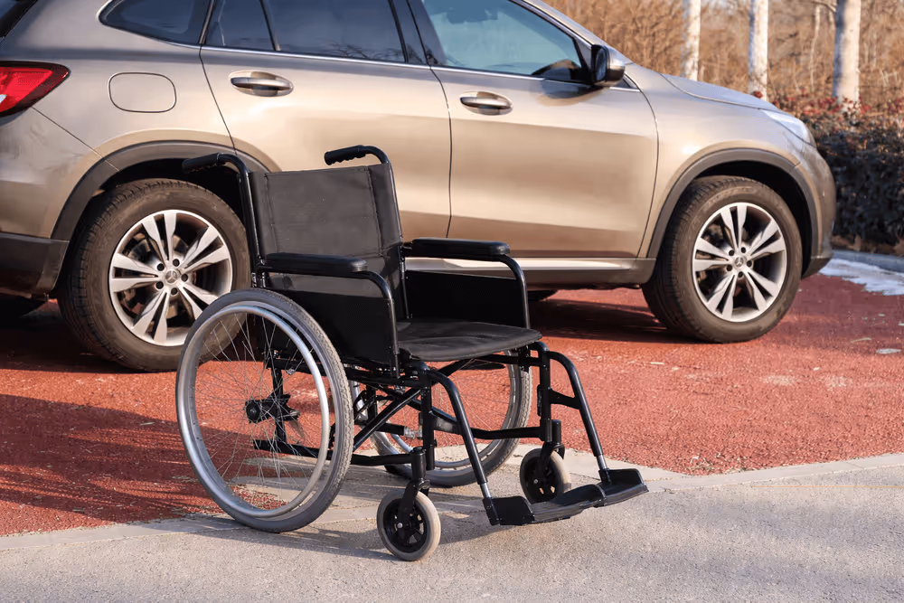 Empty black wheelchair on pavement with a beige SUV parked behind it.