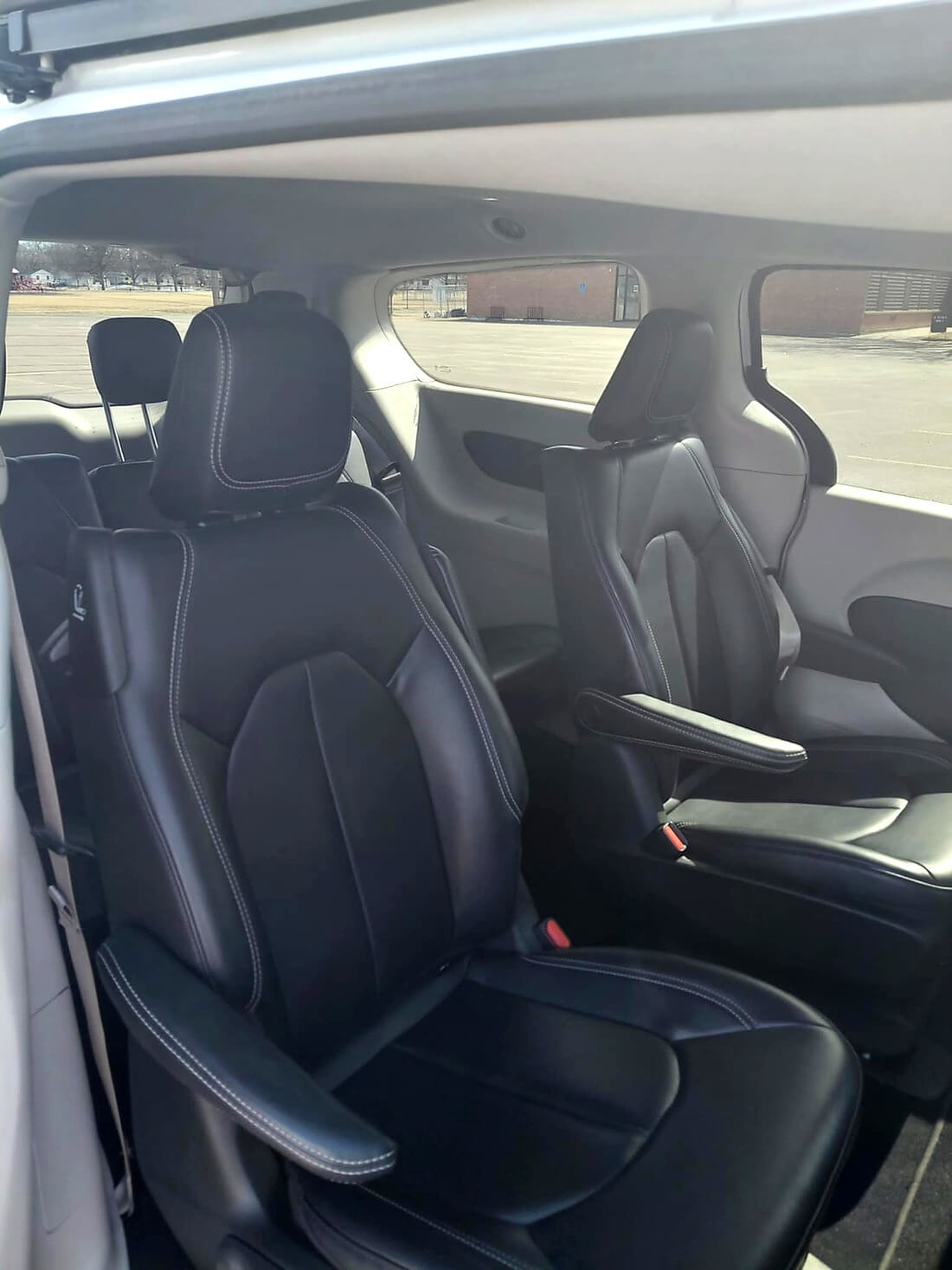 Interior view of a vehicle showing two black leather captain seats with armrests and white stitching.