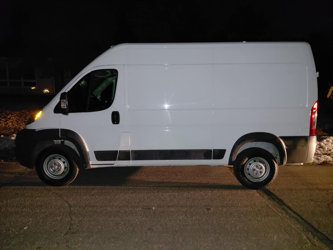 Residential backyard with a winding dry creek bed made of smooth white stones, green grass, rose bushes, and houses under a partly cloudy sky.