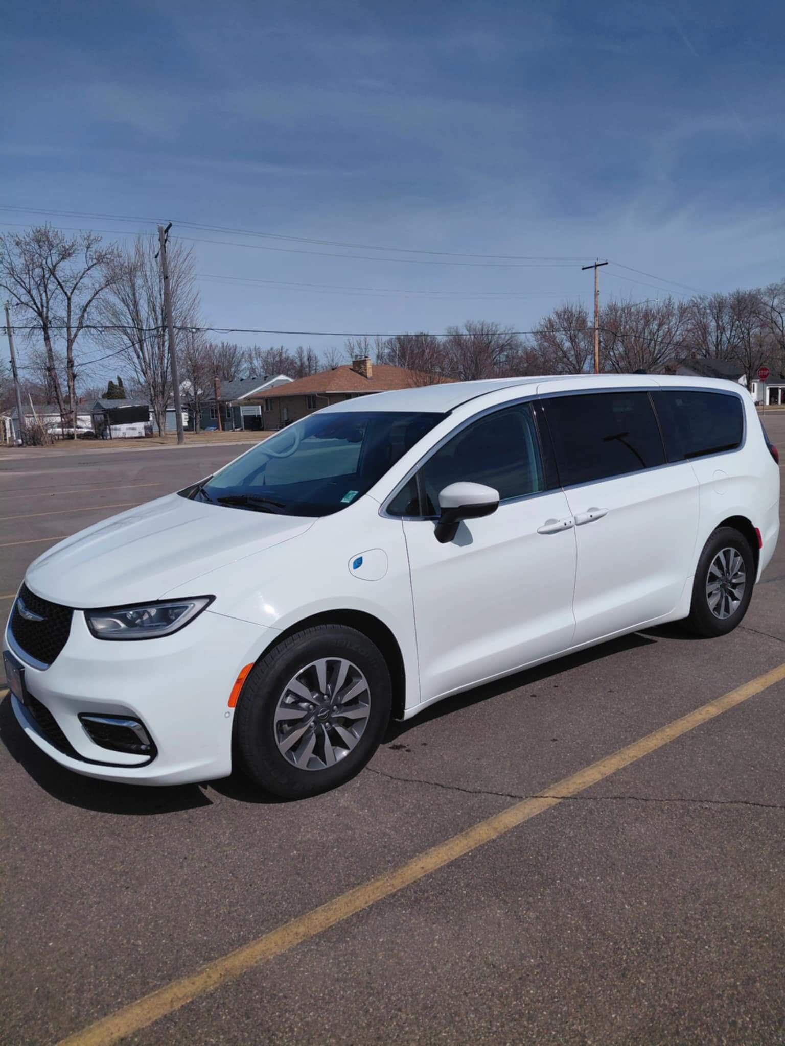 Construction site with workers assembling a gray concrete block retaining wall beside a house, surrounded by trees and gravel.