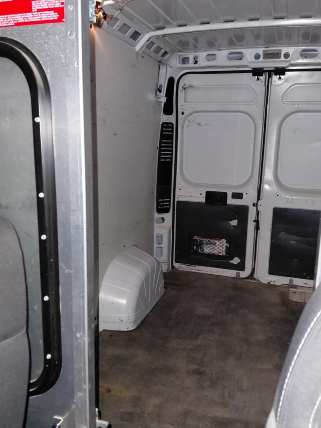 Empty cargo area inside a white transport van showing rear doors and wheel well.