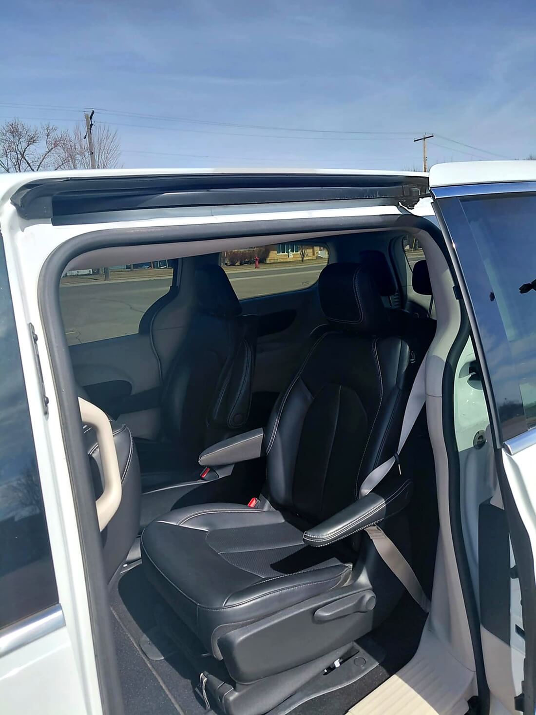 Curved paved walkway with light and dark gray bricks leading to a black metal garden gate surrounded by bare soil and bushes.
