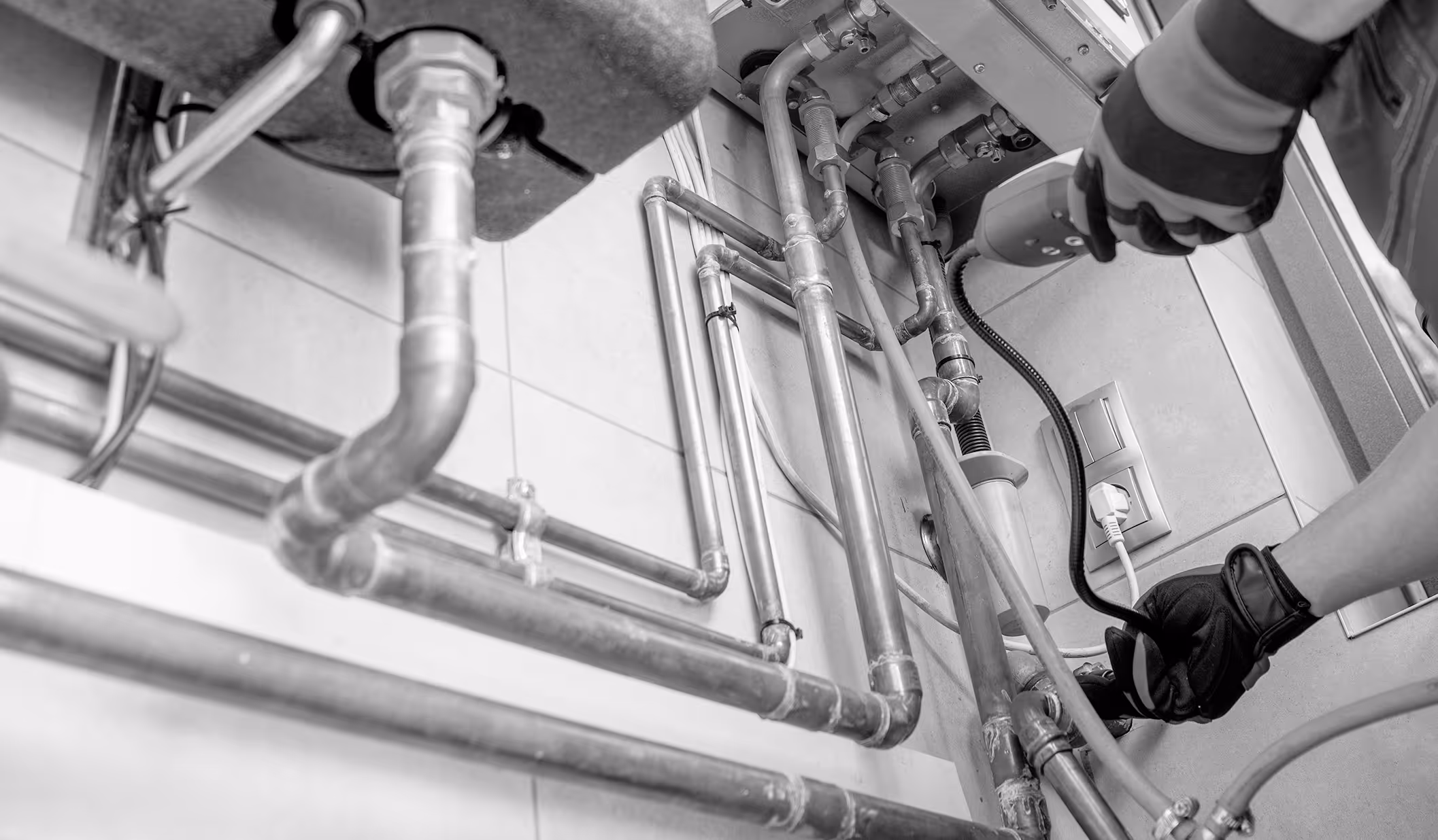 Person wearing gloves using a handheld tool to inspect or repair plumbing pipes under a sink.