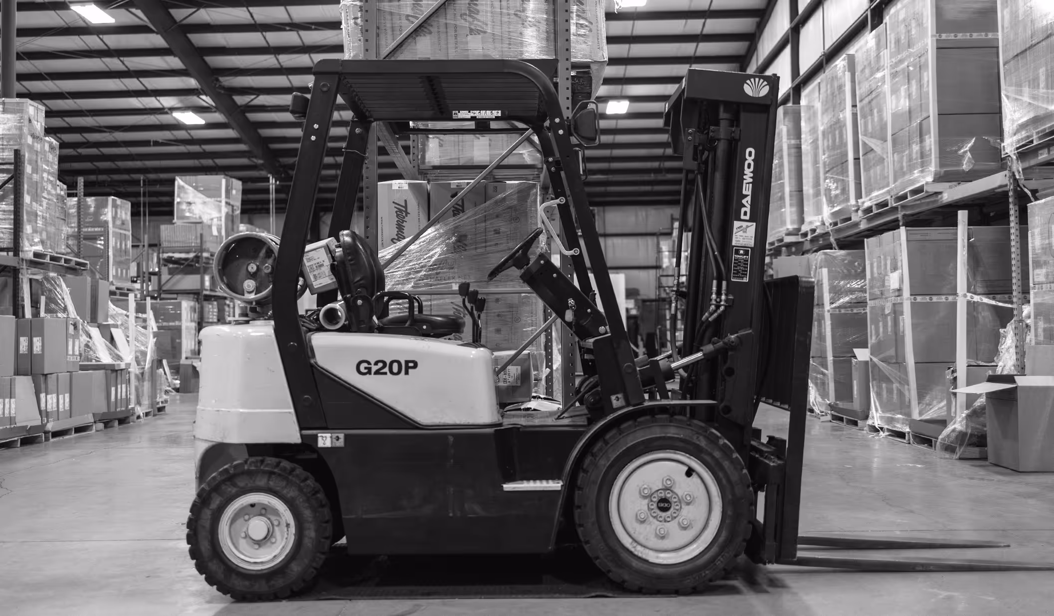 Black and white photo of a forklift inside a warehouse with shelves stacked with boxes.