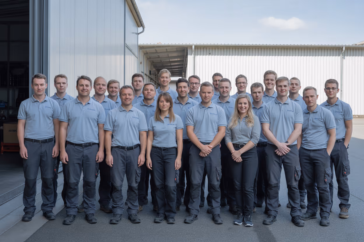 Eine Gruppe von 22 Personen einer Entrümpelungsfirma, überwiegend Männer, steht in Arbeitskleidung vor einem Industriegebäude und blickt in die Kamera.