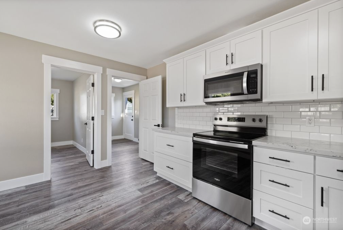 Modern kitchen with white cabinets, stainless steel oven and microwave, white subway tile backsplash, and wood laminate flooring.