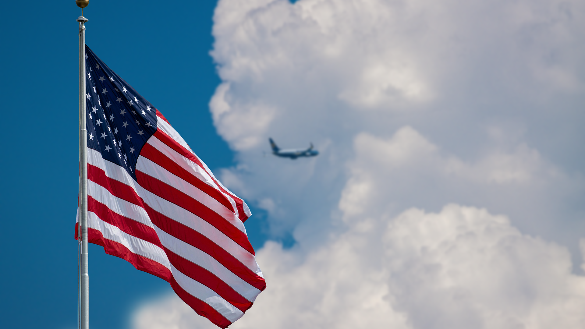 an american flag waving in the wind while a plane is flying in the background