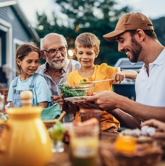 Retiree eating dinner with their children and grandchildren outside their house