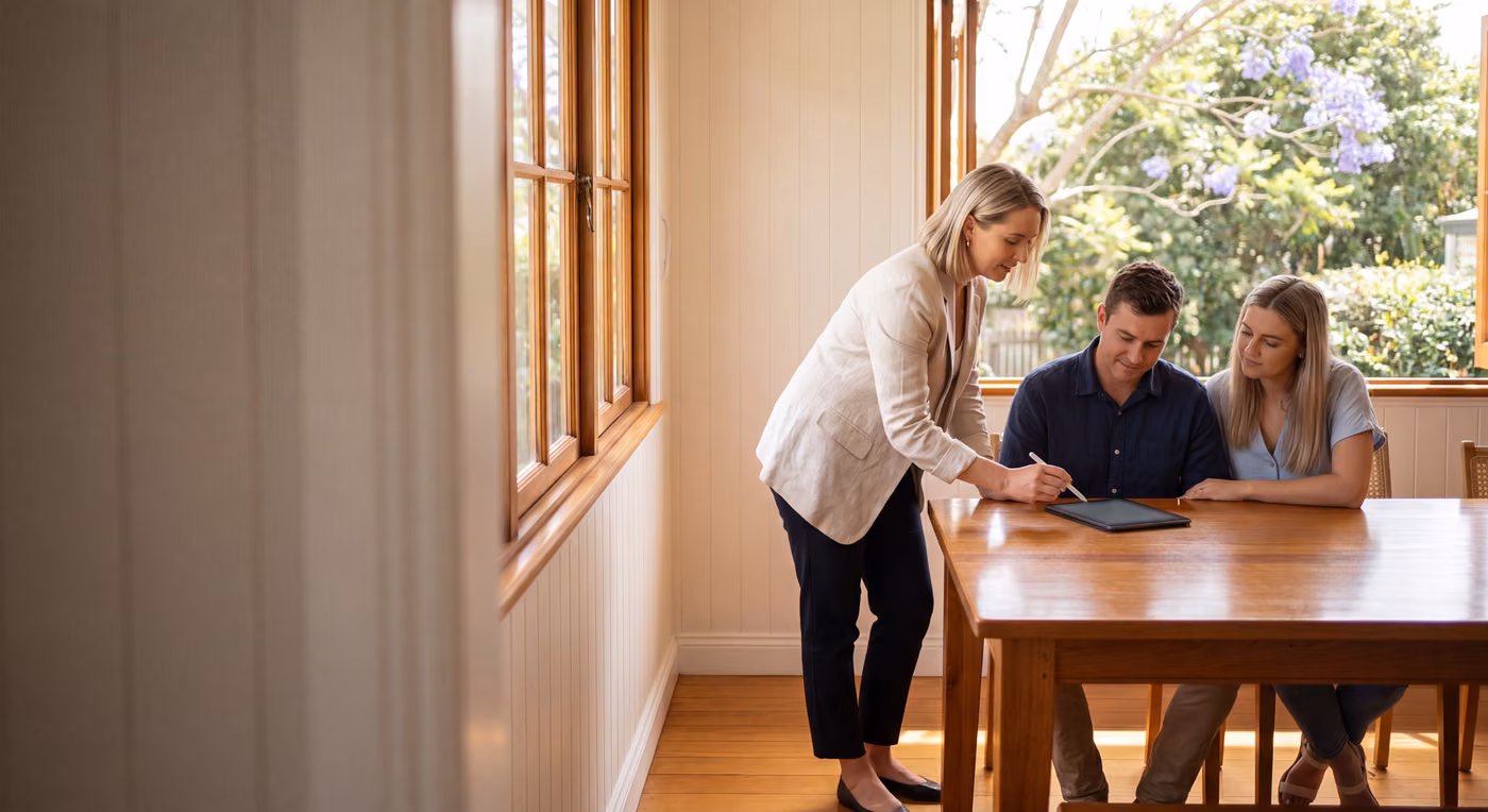 Real estate agent guiding a couple through signing a residential sales contract on a tablet at a dining table