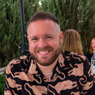 A head shot of the game designer, Ted Mann Schaller, wearing a black shirt with pink and tan tigers.