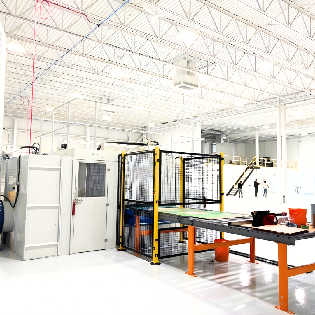Modern industrial workspace with machinery, bright white walls, and three people walking near stairs in the background.